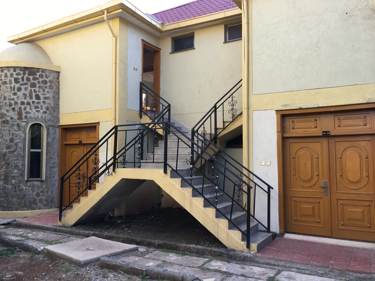 Exterior staircase with black iron railings beside a stone tower and wooden doors